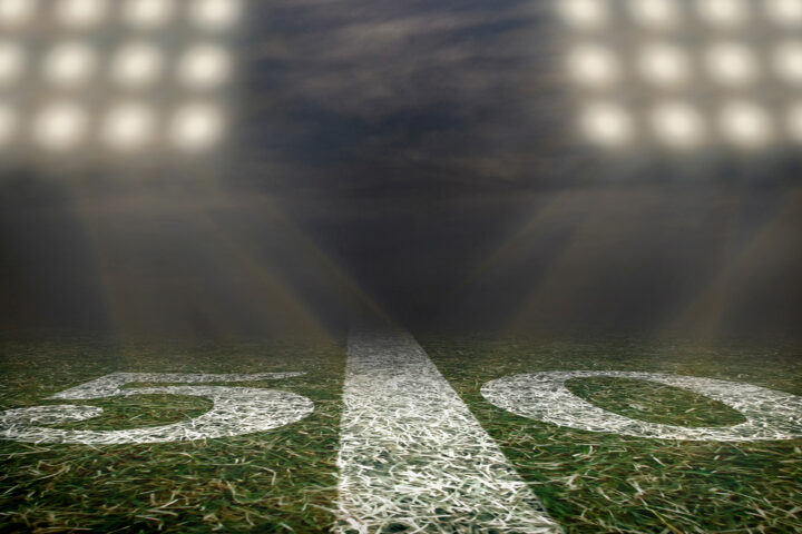 Football field at night, with stadium lights highlighting the 50 yard line.